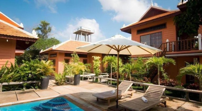 Piscina exterior con tumbonas y sombrilla del Sambopich Chenla Hotel rodeada de jardines tropicales