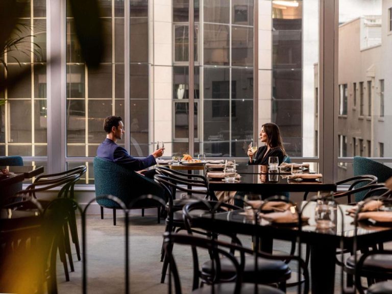 Pareja cenando con copa de vino en el elegante restaurante del Swissotel Sydney con vistas a la ciudad