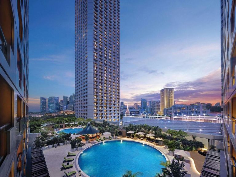 Piscina exterior al atardecer con vistas a la torre del Swissotel The Stamford Singapore