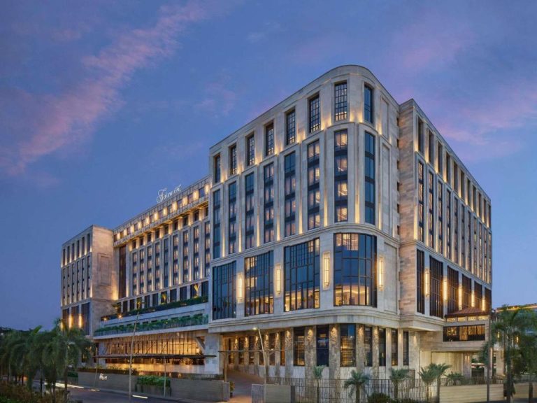 Fachada exterior iluminada del Fairmont Mumbai al atardecer con arquitectura de lujo y palmeras