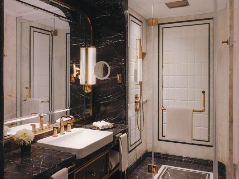 Baño de lujo con mármol negro y detalles dorados en el Fairmont Mumbai, con ducha y lavabo elegante