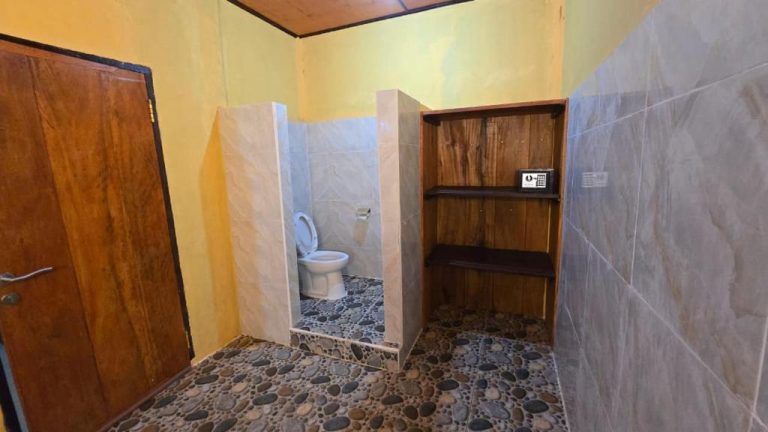 Baño privado con inodoro, suelo de piedra natural y estantería de madera en Tangkoko Sanctuary Villa