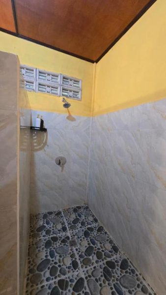 Ducha con suelo de piedras naturales y azulejos grises en el baño de Tangkoko Sanctuary Villa