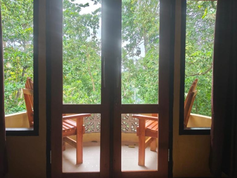 Terraza con sillas de madera y vistas al jardín tropical en Tangkoko Sanctuary Villa