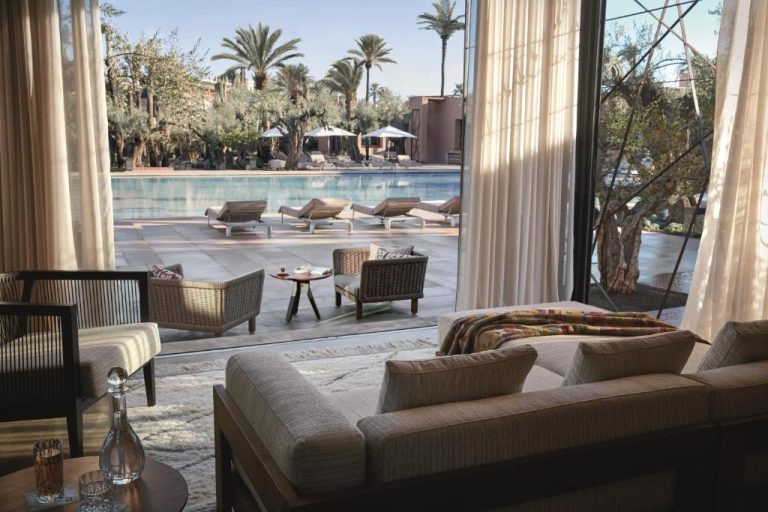 Lujoso salón con sofás y vistas a la piscina exterior rodeada de palmeras en Royal Mansour Marrakech