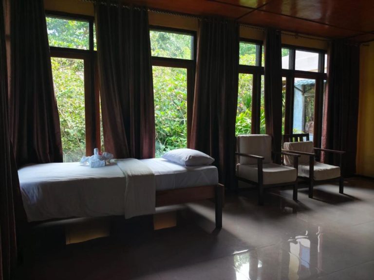 Habitación con cama individual y sillones con vistas al jardín tropical en Tangkoko Sanctuary Villa