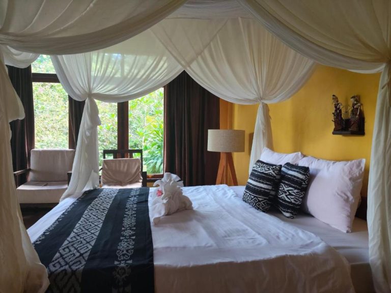Habitación con cama de dosel y vistas a jardín tropical en Tangkoko Sanctuary Villa