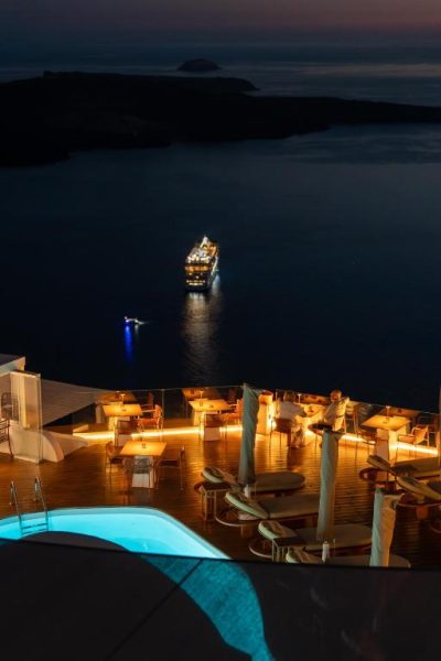 Terraza con piscina iluminada y vistas nocturnas a la caldera de Santorini en Sun Rocks Boutique Hotel