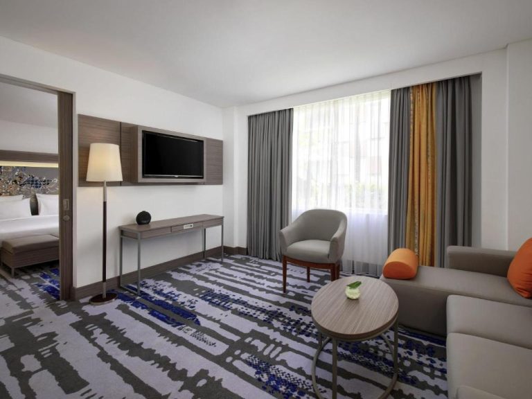 Salón de suite con sofá, mesa y TV del Novotel Bali Ngurah Rai Airport con dormitorio separado