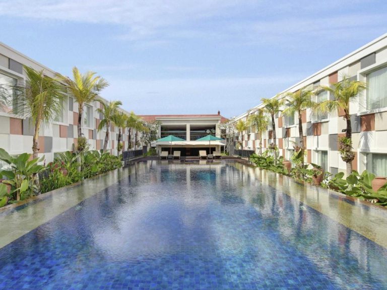 Piscina exterior larga con palmeras tropicales del Novotel Bali Ngurah Rai Airport rodeada de jardines