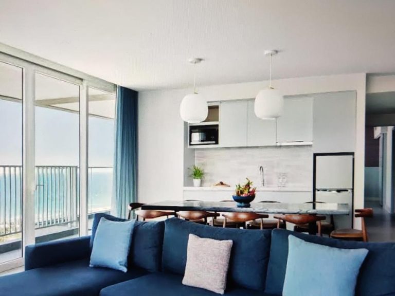 Salón con sofá azul y cocina integrada con vistas al mar en The Manito Seaview Suites