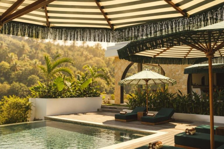 Piscina infinita con tumbonas y sombrillas de rayas en Kanalla Boutique Hotel rodeado de vegetación tropical