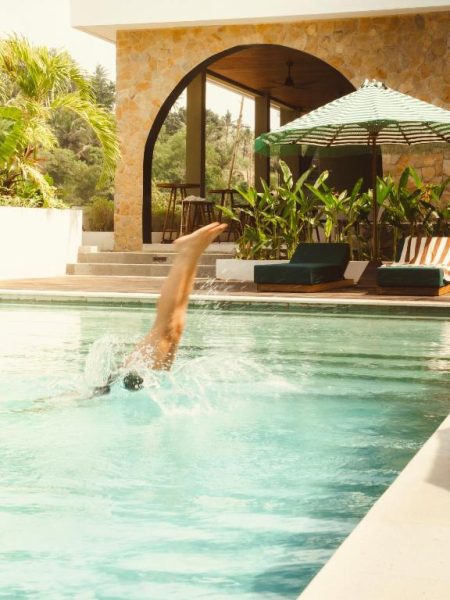 Persona zambulléndose en la piscina exterior del Kanalla Boutique Hotel con tumbonas y sombrilla verde