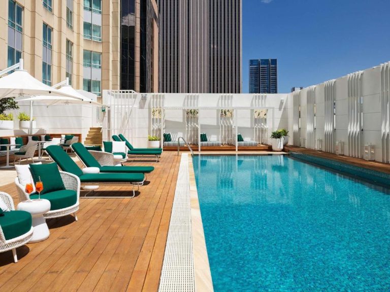 Piscina exterior en terraza con tumbonas verdes y vistas a los rascacielos del Swissotel Sydney