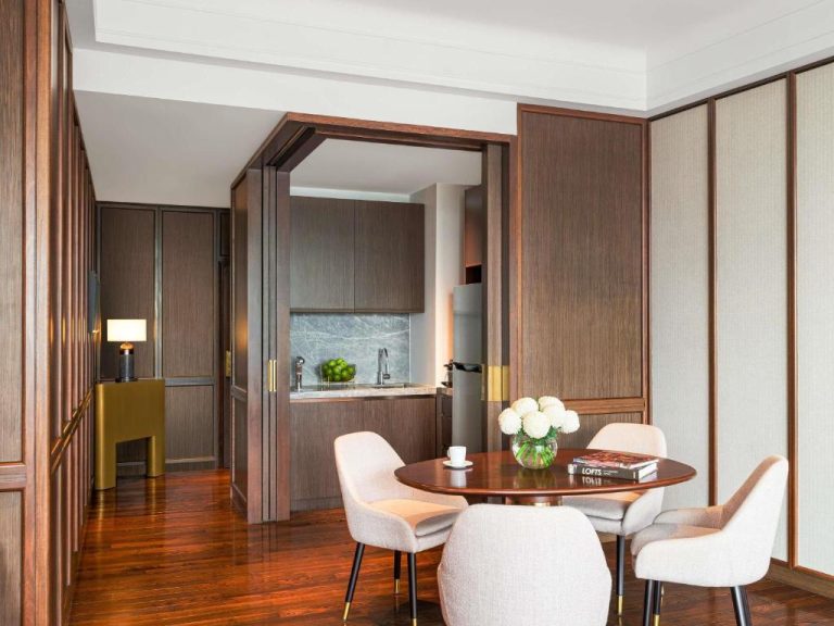 Suite con comedor elegante y cocina integrada en el Fairmont Singapore, decoración en madera y flores blancas