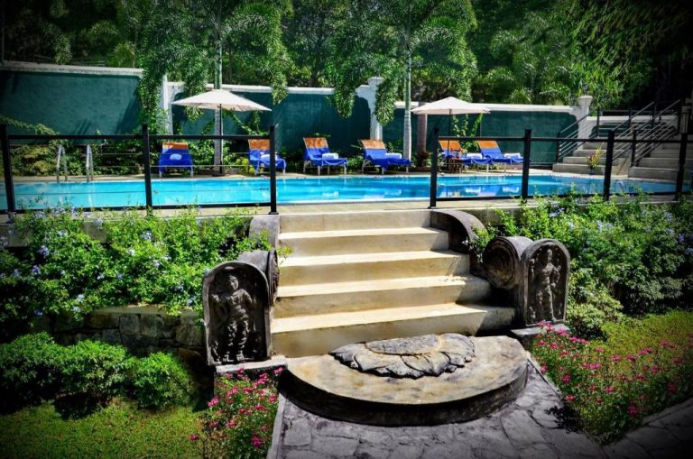 Piscina exterior con jardines tropicales y esculturas de piedra en The Kings Villa