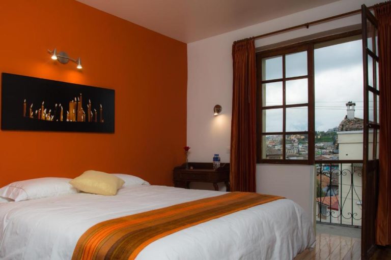 Habitación doble con pared naranja y balcón con vista panorámica en Hotel Casa Ecuatreasures Centro Histórico