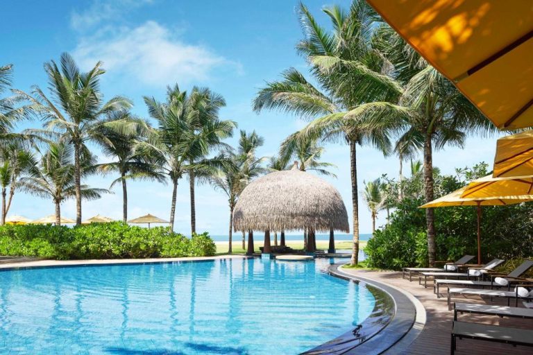 Piscina exterior con palmeras y gazebo de paja frente al mar en Sentido Heritance Negombo