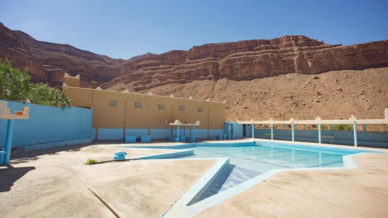 Piscina exterior del Kasbah Hotel Camping Jurassique rodeada de montañas rocosas desérticas en Marruecos