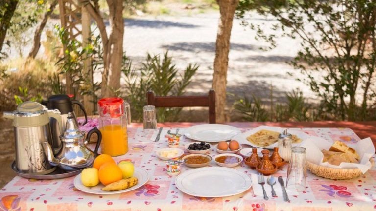 Desayuno tradicional marroquí servido al aire libre en Kasbah Hotel Camping Jurassique con zumo, pan y frutas