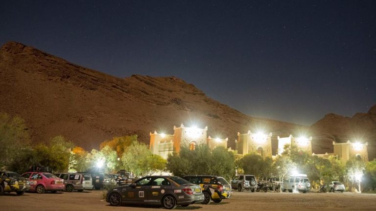 Vista nocturna del Kasbah Hotel Camping Jurassique iluminado entre montañas del desierto bajo un cielo estrellado