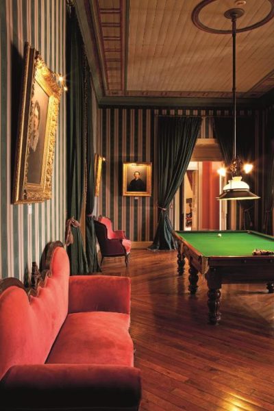 Elegante sala de billar vintage con sofás rojos y retratos en Hotel Casa Real Viña Santa Rita