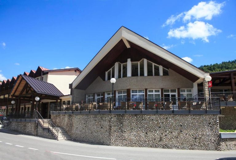 Fachada exterior del Hotel Djokovic con terraza y muro de piedra bajo cielo azul