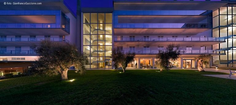 Fachada exterior iluminada del Eureka Palace Hotel Spa Resort con jardín y árboles por la noche