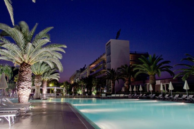 Piscina exterior iluminada de noche con palmeras y tumbonas del Eureka Palace Hotel Spa Resort