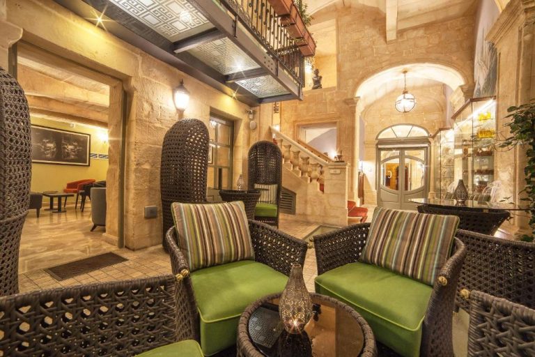 Elegante lobby con sillones de ratán y cojines verdes en Palazzo Consiglia IK Collection Malta