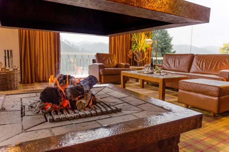 Salón con chimenea central encendida y sofás de cuero del Lago Azul Eco Hotel con vistas a la montaña