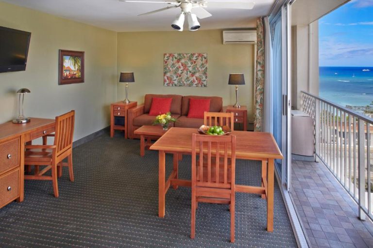 Suite con salón, mesa de comedor y balcón con vistas al mar en Pacific Monarch Hotel Waikiki