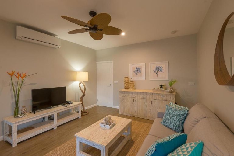 Sala de estar con sofá, televisión y ventilador de techo estilo tropical en Le Nautique Waterfront Hotel La Digue