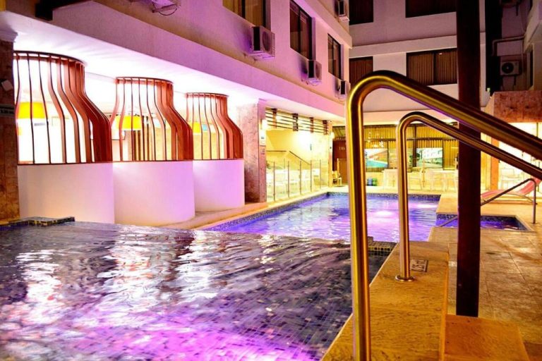 Piscina interior iluminada con luces moradas del Hotel La Riviera, con barandilla dorada y zona de descanso