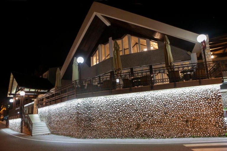 Terraza exterior iluminada del Hotel Djokovic con muro de piedra y sombrillas durante la noche