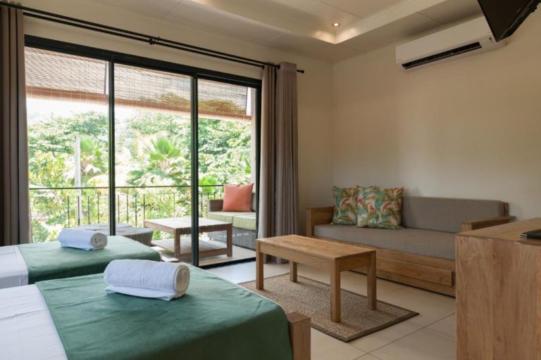 Habitación doble con camas verdes, sofá y balcón con vistas a jardín tropical en Le Repaire Boutique Hotel