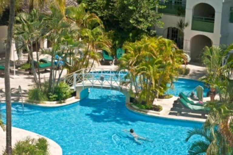 Piscina exterior con puente blanco y palmeras tropicales del Mango Bay All Inclusive Barbados