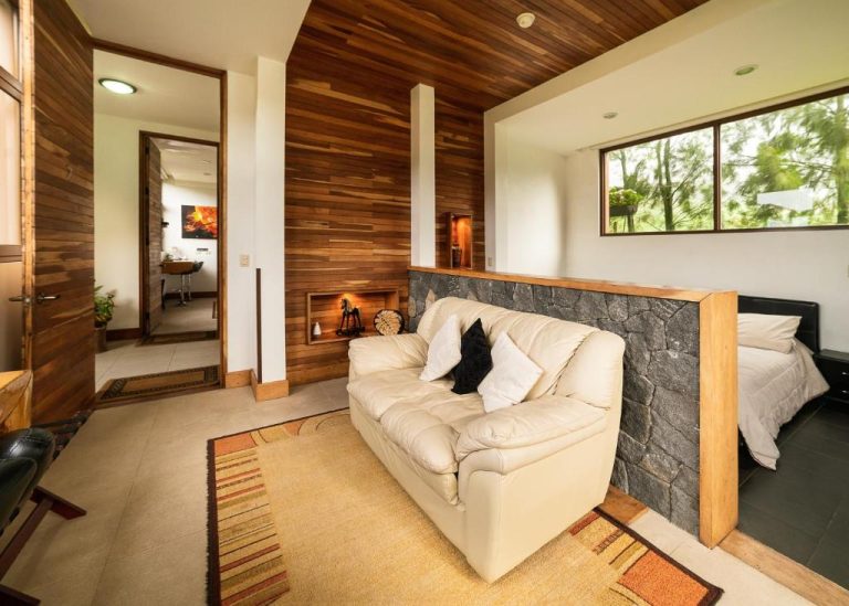 Suite del Altura Hotel con sofá de cuero blanco, revestimiento de madera y zona de descanso con pared de piedra