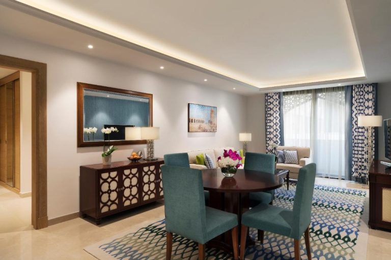 Salón comedor elegante con mesa redonda y sillas turquesa en Al Najada Doha Hotel Apartments by Oaks