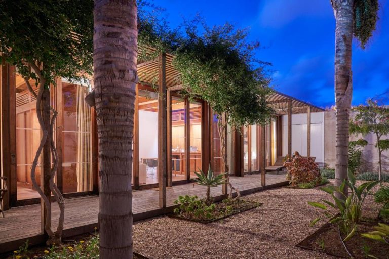Jardín exterior con terraza de madera y vegetación tropical del Hotel Porto Santo & Spa al atardecer