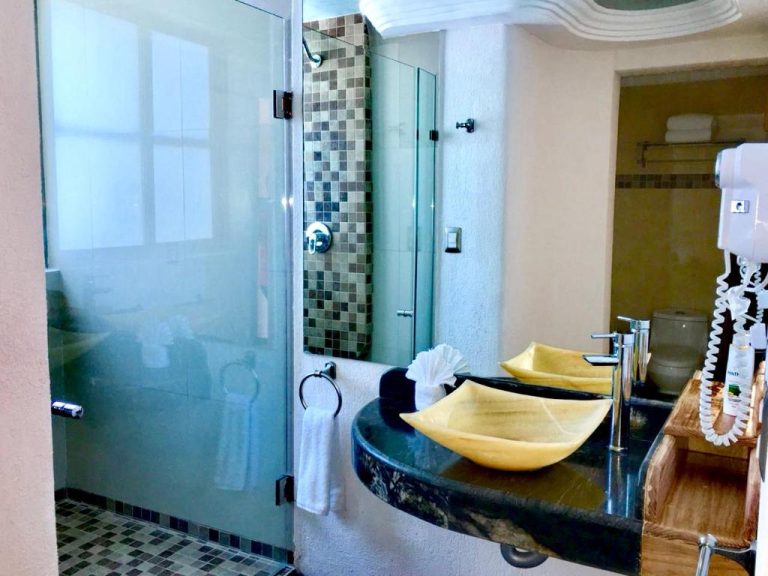 Baño moderno con lavabos de mármol amarillo y ducha de cristal en Hotel Blue Star Cancun