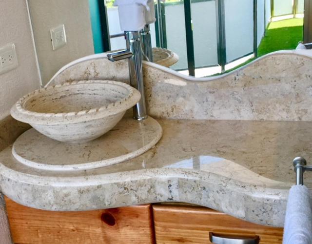 Lavabo artesanal de mármol travertino con encimera ondulada en el baño del Hotel Blue Star Cancun