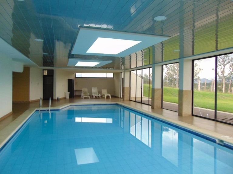 Piscina interior climatizada del Quito Airport Suites Hotel con grandes ventanales y vistas al jardín