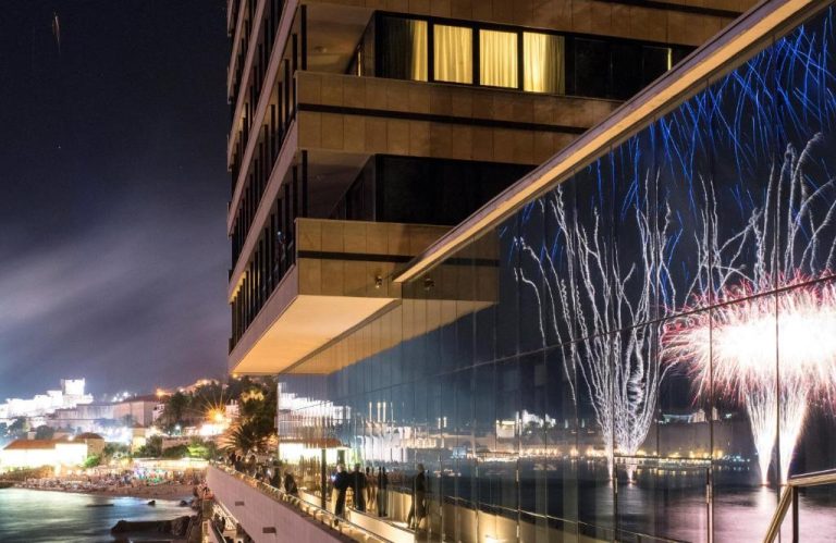 Vista nocturna de la terraza del Hotel Excelsior con fuegos artificiales reflejados en fachada de cristal