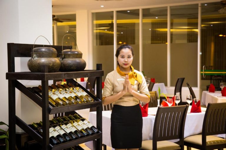 Recepcionista del Glorious Hotel dando la bienvenida en el restaurante con estantería de vinos