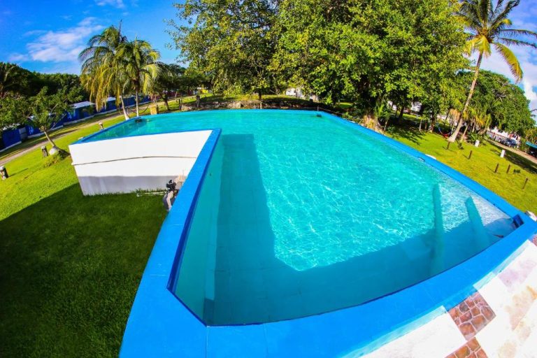 Piscina exterior de aguas cristalinas rodeada de palmeras y jardín tropical en ECO-CABAÑAS Cancún