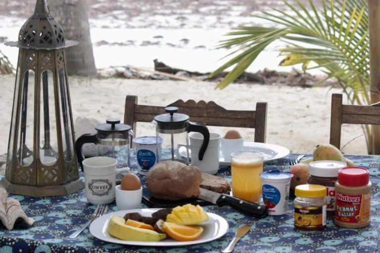 Desayuno completo con frutas, pan, huevos y café frente a la playa en Sawa Sawa Beach House