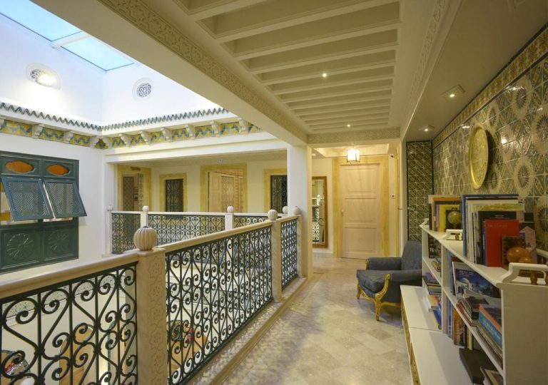 Corredor interior del Riad Dar Alouini con balcón de forja, estanterías y decoración árabe tradicional