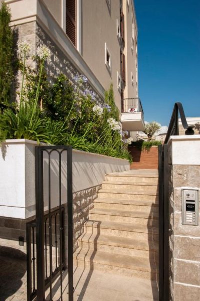 Entrada principal con escaleras de piedra y jardín con flores del Hotel Vela