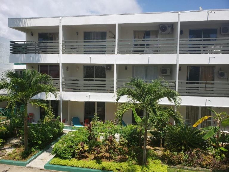 Fachada exterior del Negril Beach Club Condos con balcones, jardín tropical y palmeras en Jamaica